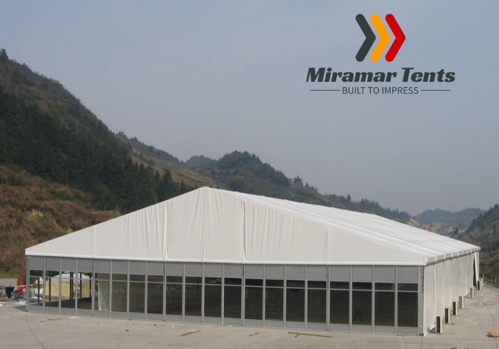Large white All-Occasion Canopy Tent with the Miramar Tents logo set up in a valley with hills in the background.