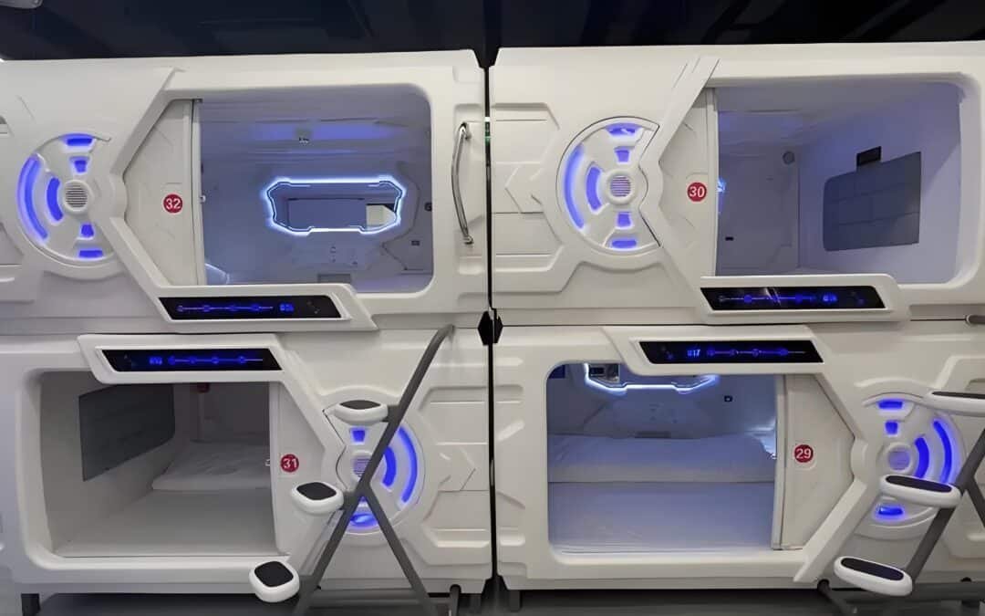 A Futuristic Capsule Hotel Pod With Blue Led Lighting, Featuring Two Stacked Sleeping Compartments, Each With A Small Ladder, Control Panel, And A Window.